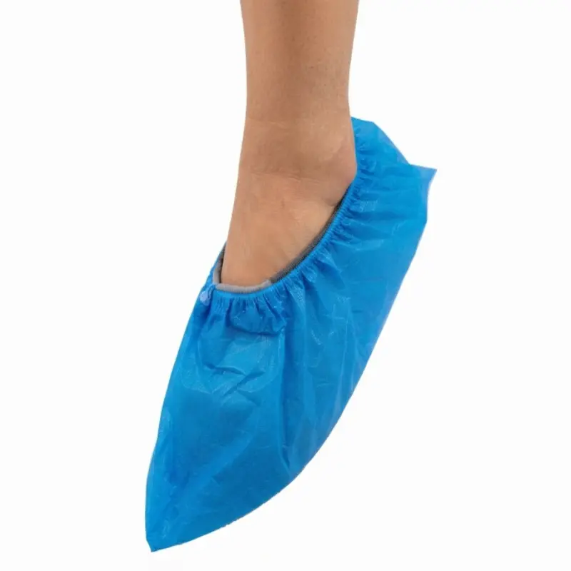 Pierna de una persona con un cubre calzado desechable de polietileno azul ajustado al pie en un entorno clínico.
