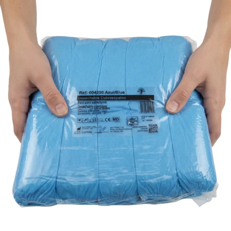 Manos de una persona sujetando un paquete sellado de cubre calzados desechables de polietileno azul.