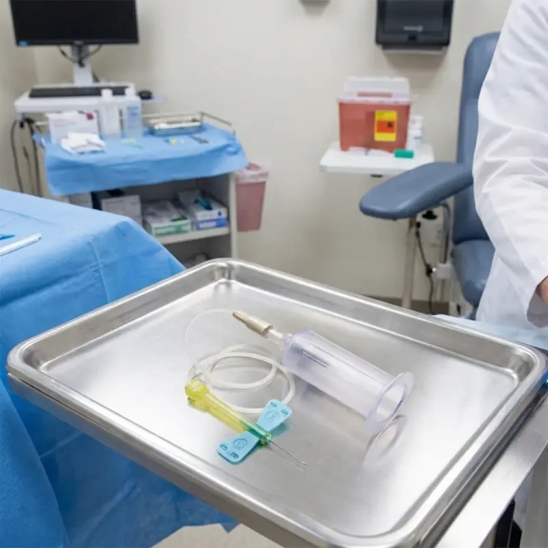 Bandeja de acero inoxidable con una palomilla Safety-Lok y portatubos en una sala de exploración médica.