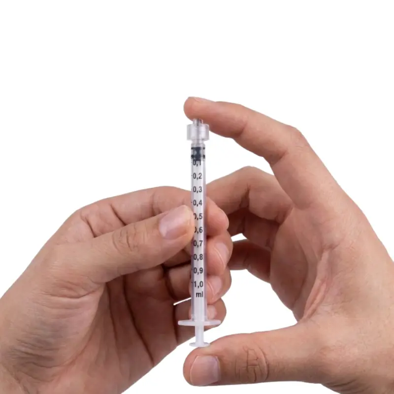 Manos sosteniendo y manipulando una jeringa de insulina transparente de 1 ml BBraun Omnifix sobre un fondo blanco aislado.