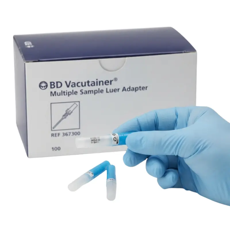 Caja de adaptadores BD Vacutainer junto a una mano con guante azul sosteniendo un adaptador y dos unidades sobre fondo blanco.