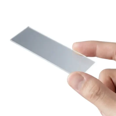 Dedos de una mano sosteniendo un portaobjetos de microscopio de vidrio transparente por los bordes.