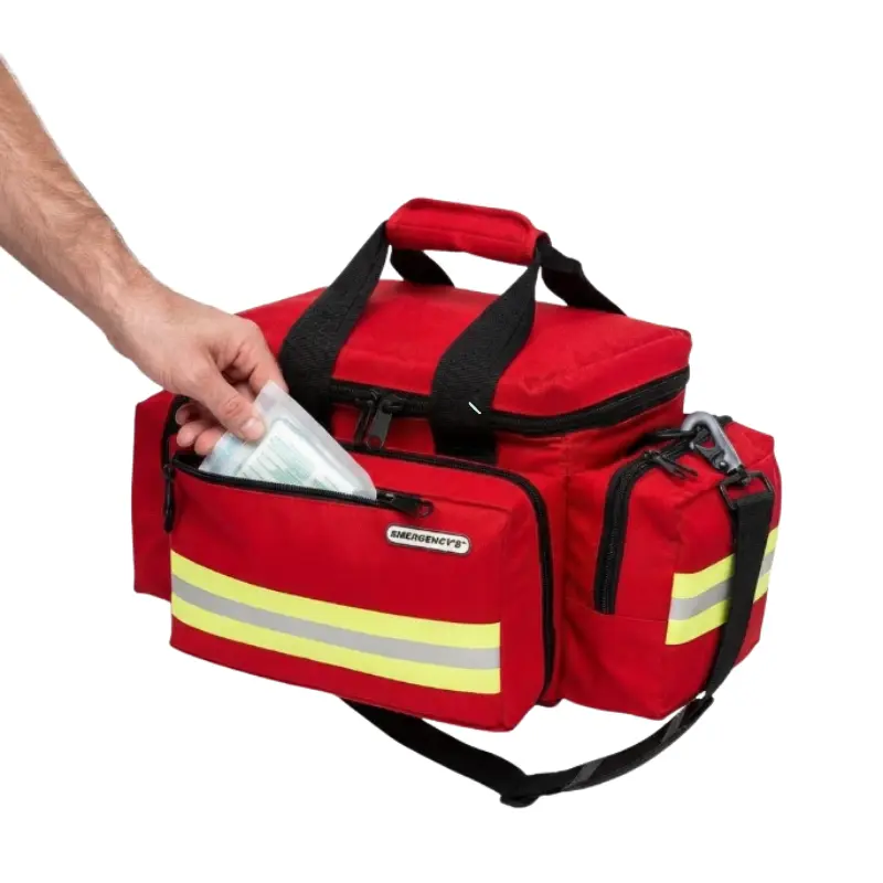 Mano introduciendo material sanitario dentro del compartimento frontal de una bolsa ligera de emergencias roja.