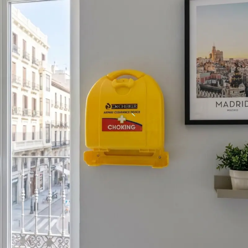 Soporte de pared amarillo con estuche Dechoker instalado en una oficina luminosa junto a un gran ventanal.