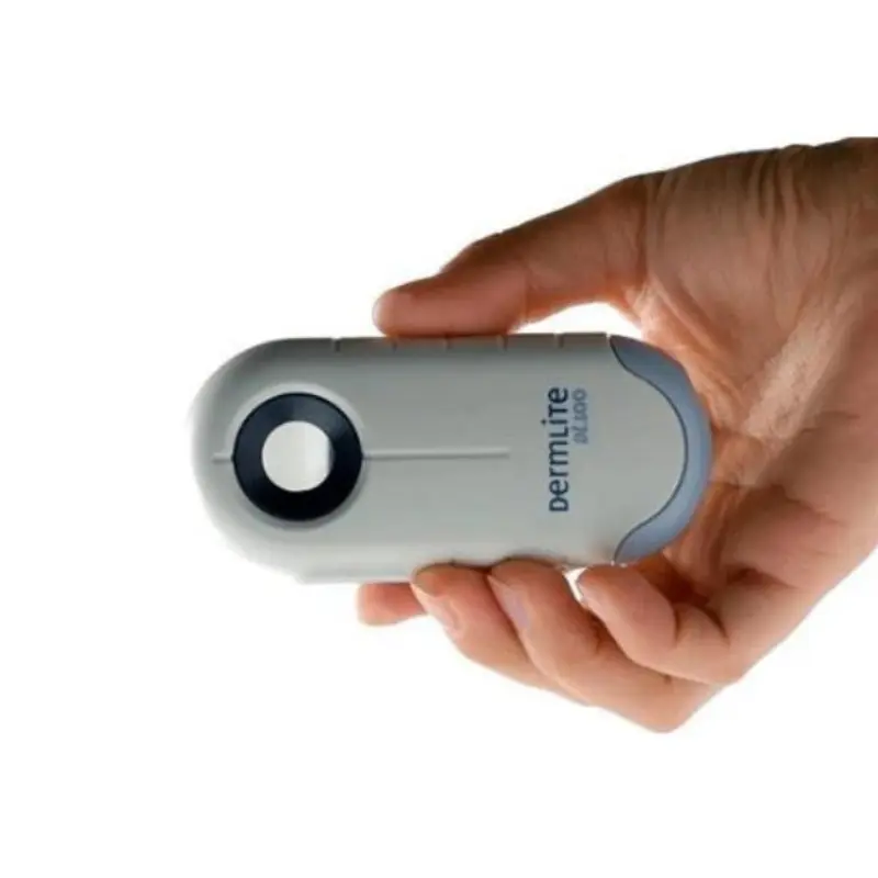 Mano sosteniendo el dermatoscopio Dermlite DL100 de luz polarizada sobre fondo blanco para mostrar su tamaño compacto.