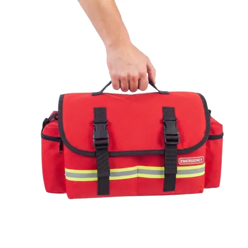 Mano sosteniendo el asa superior de la bolsa ligera SOFT de emergencias roja con cierres de hebilla negra.