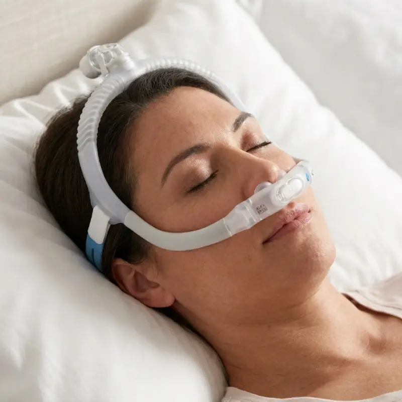 Mujer durmiendo relajadamente en una almohada blanca utilizando la máscara nasal ResMed AirFit P30i para la apnea.