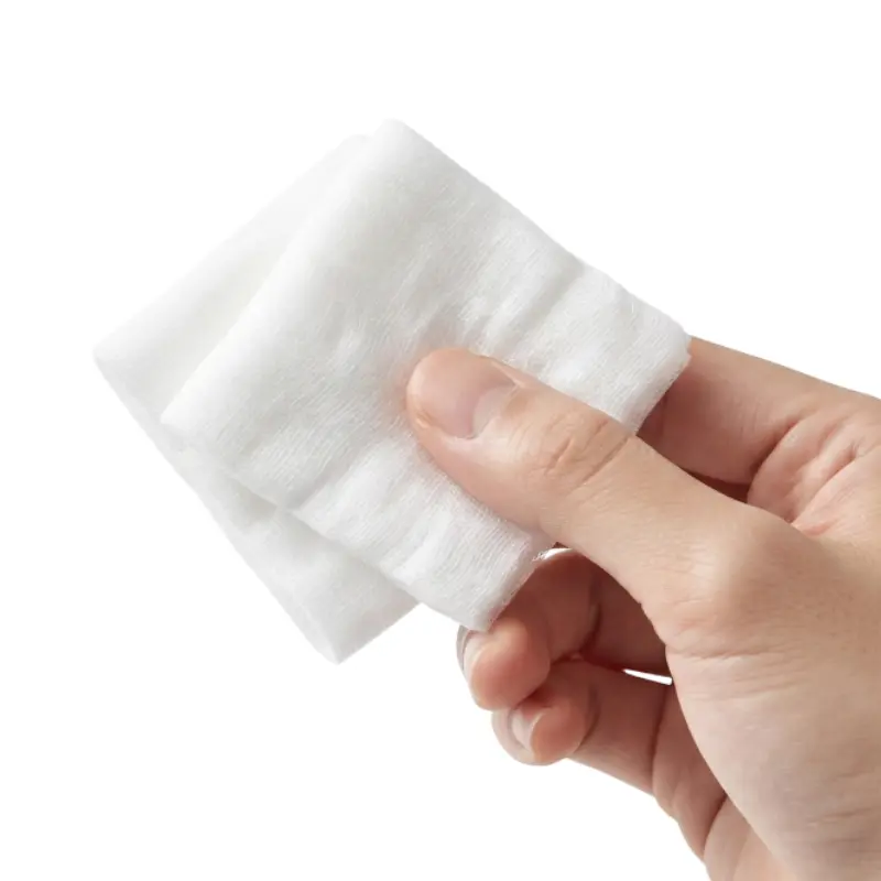 Mano sosteniendo una gasa de algodón estéril doblada en color blanco sobre un fondo claro.
