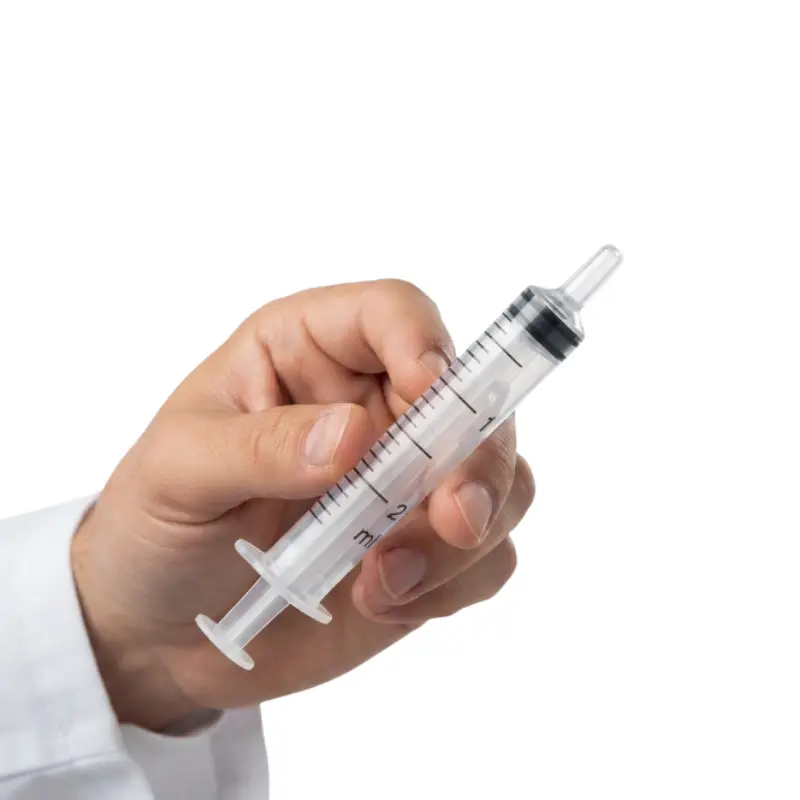 Mano de un profesional sanitario sosteniendo una jeringa de 3 cuerpos de 2 ml con graduación visible sobre fondo blanco.