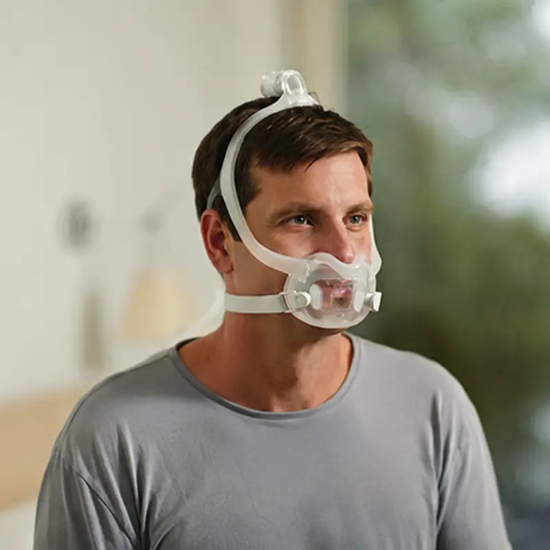 Hombre sonriente usando una máscara facial Philips Dreamwear Full Face en talla L durante una terapia CPAP.