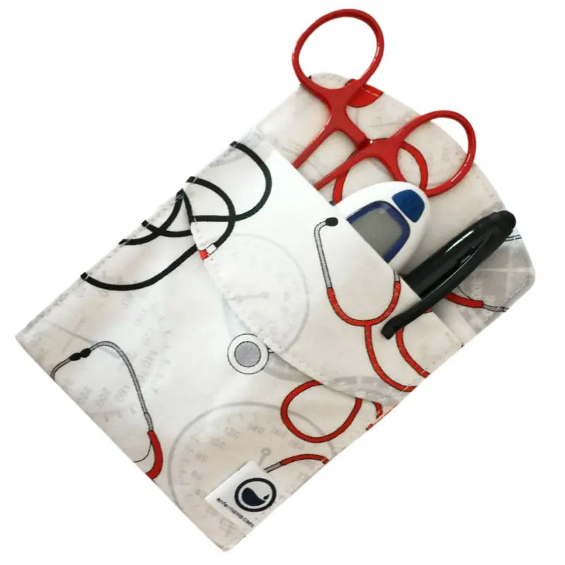 Salvabolsillos sanitario blanco con estampado de fonendoscopios y tensiómetros, equipado con tijeras y bolígrafo.