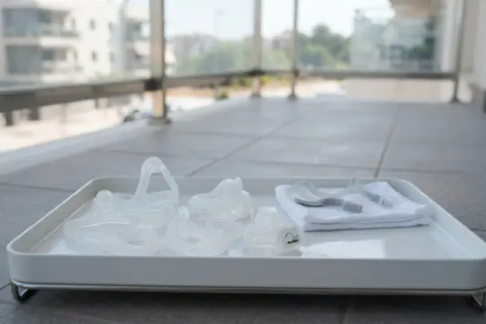 Bandeja blanca con componentes de CPAP limpios situada en el suelo de un balcón luminoso con vistas a edificios.