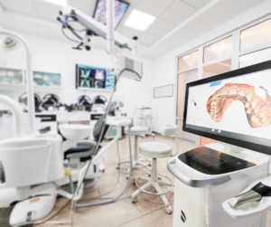 Primer plano de un monitor mostrando un escaneo digital 3D de una dentadura humana en un consultorio odontológico moderno y luminoso equipado con tecnología avanzada.