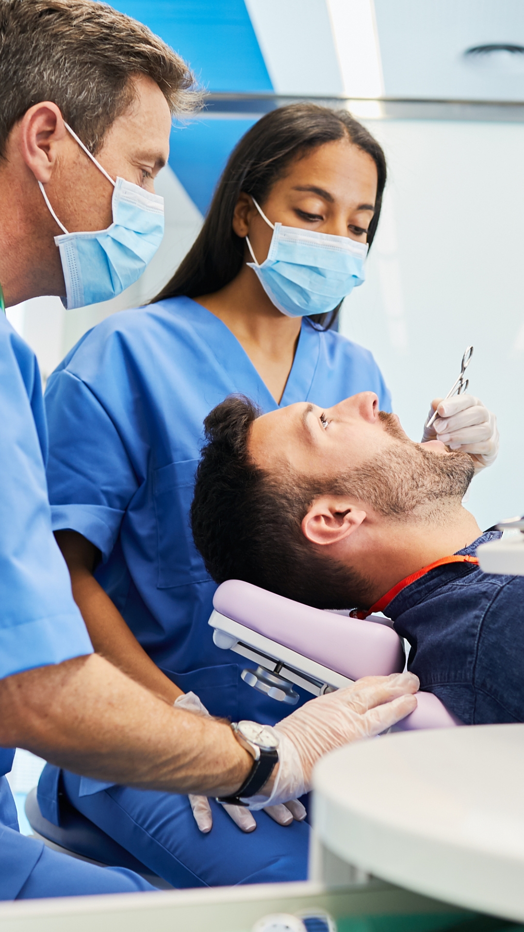 Texto alternativo: Un odontólogo y su asistente realizan un procedimiento dental a un paciente en un sillón clínico, cumpliendo con los estándares de seguridad y acceso al paciente exigidos por la normativa de sedación.