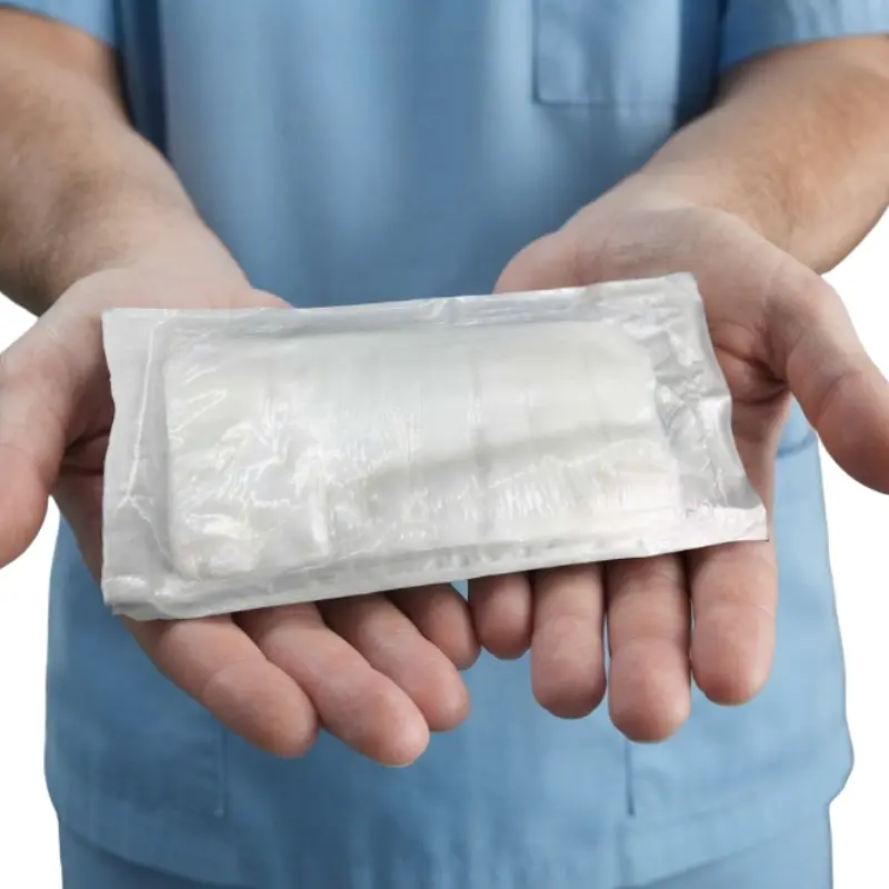 Personal sanitario con uniforme azul sosteniendo un apósito quirúrgico estéril empaquetado en sus manos.