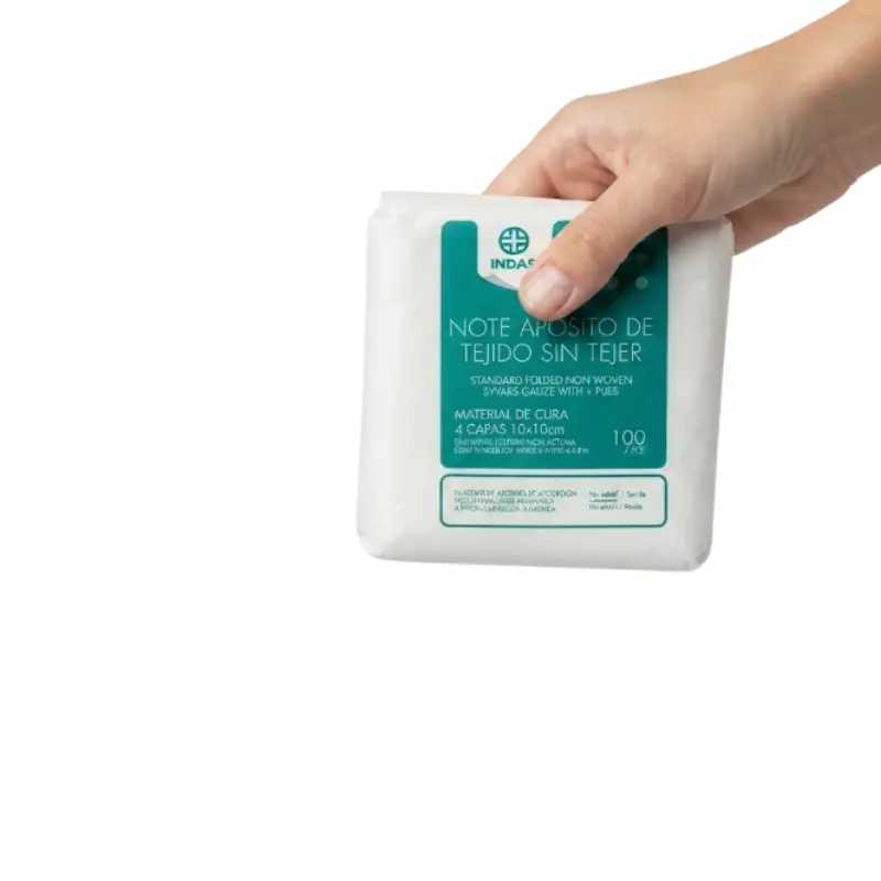 Mano sosteniendo un paquete blanco de apósitos de gasa de tejido sin tejer no estéril de 10x10 cm con etiqueta verde de Indas.