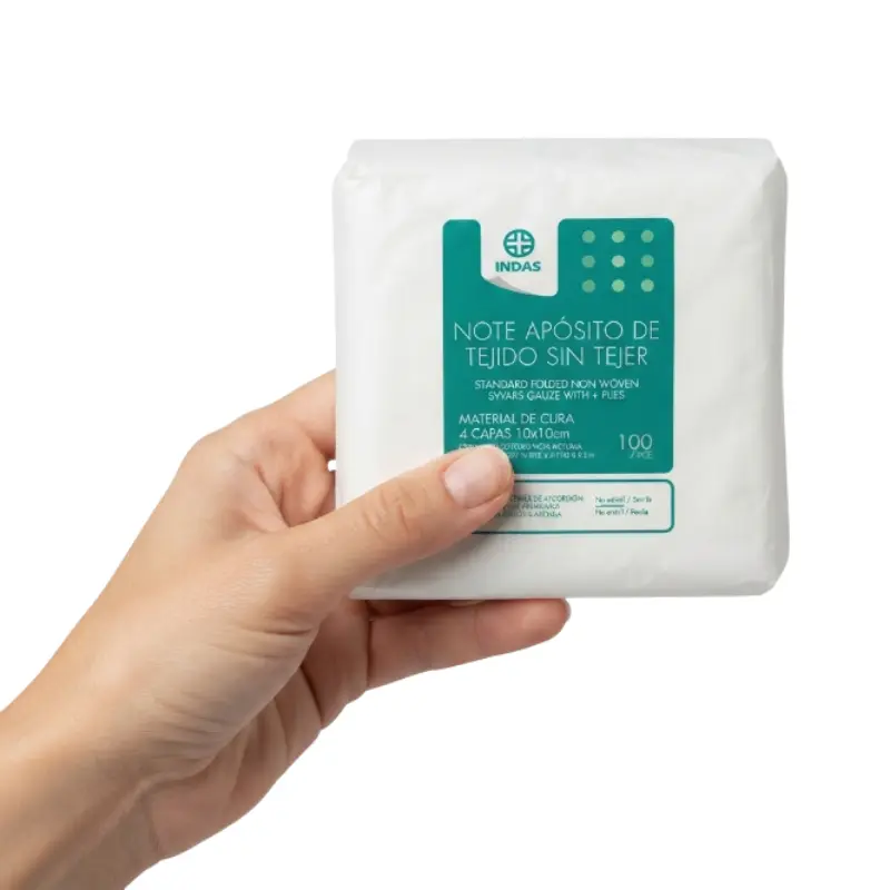 Mano sosteniendo un paquete blanco de apósitos de gasa de tejido sin tejer no estéril de 10x10 cm con etiqueta verde de Indas.