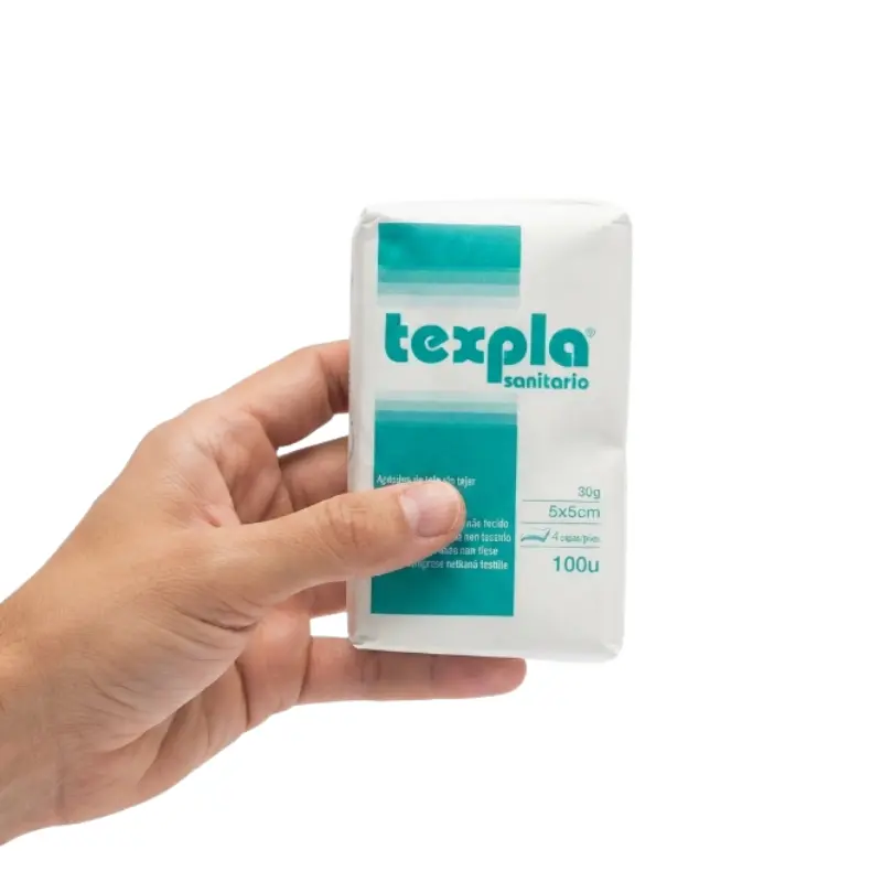 Mano sosteniendo un paquete blanco de apósitos de gasa de tejido sin tejer no estéril de 5x5 cm con detalles en verde.
