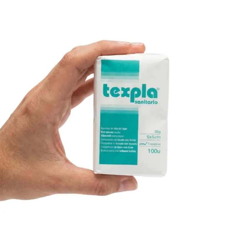 Mano sosteniendo un paquete blanco de apósitos de gasa de tejido sin tejer no estéril de 5x5 cm con detalles en verde.