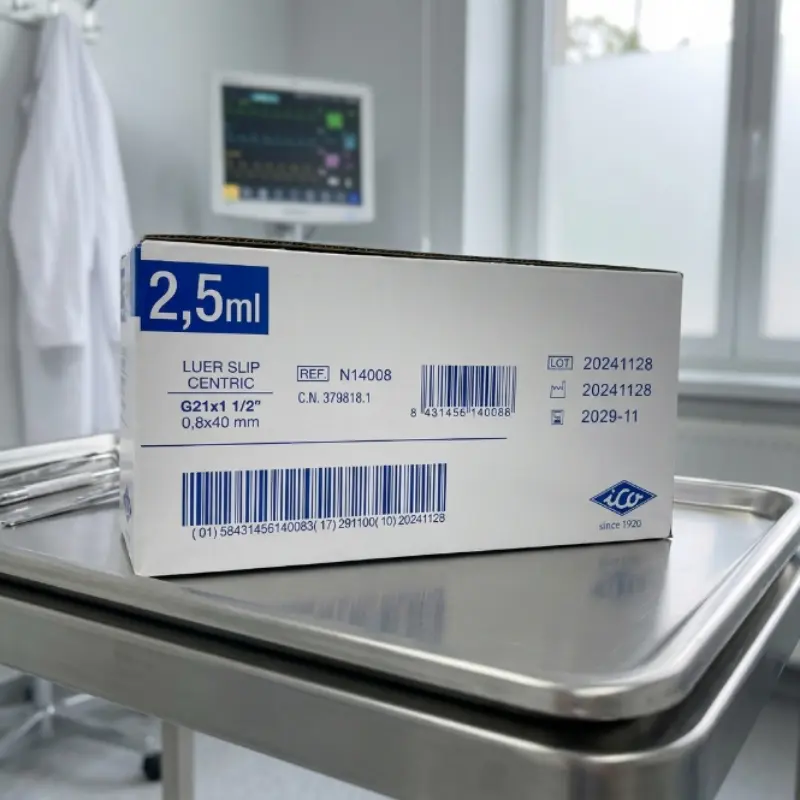Caja de jeringas ICOplus3 de 2,5 ml sobre una bandeja de acero inoxidable en una consulta médica con monitor al fondo.