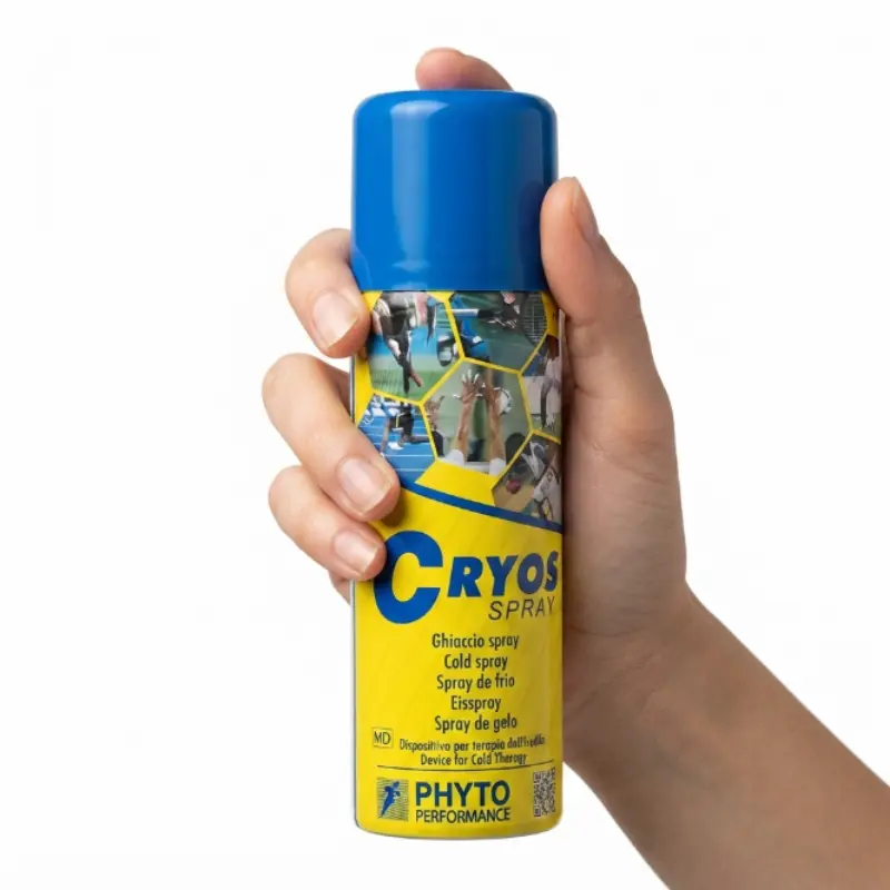 Mano sosteniendo un envase de spray de frío Cryos Árnica amarillo sobre un fondo blanco neutro.