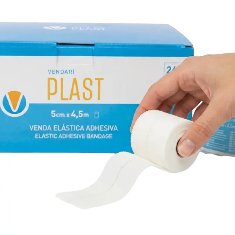 Mano sosteniendo un rollo de venda elástica adhesiva blanca Vendari PLAST frente a su caja dispensadora azul.