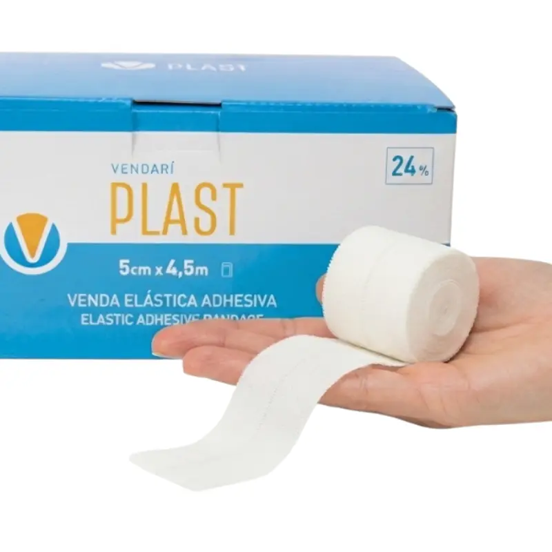 Mano de perfil sosteniendo un rollo de venda elástica adhesiva blanca Vendari PLAST con su caja azul al fondo.
