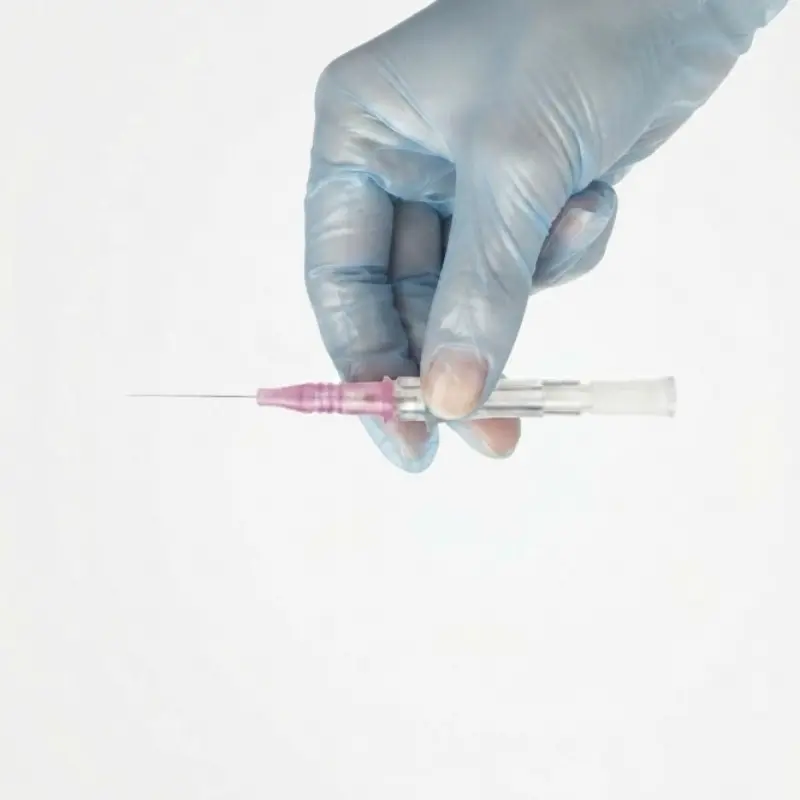 Mano con guante azul de examen sosteniendo de forma horizontal el catéter intravenoso BD Insyte 20GA.