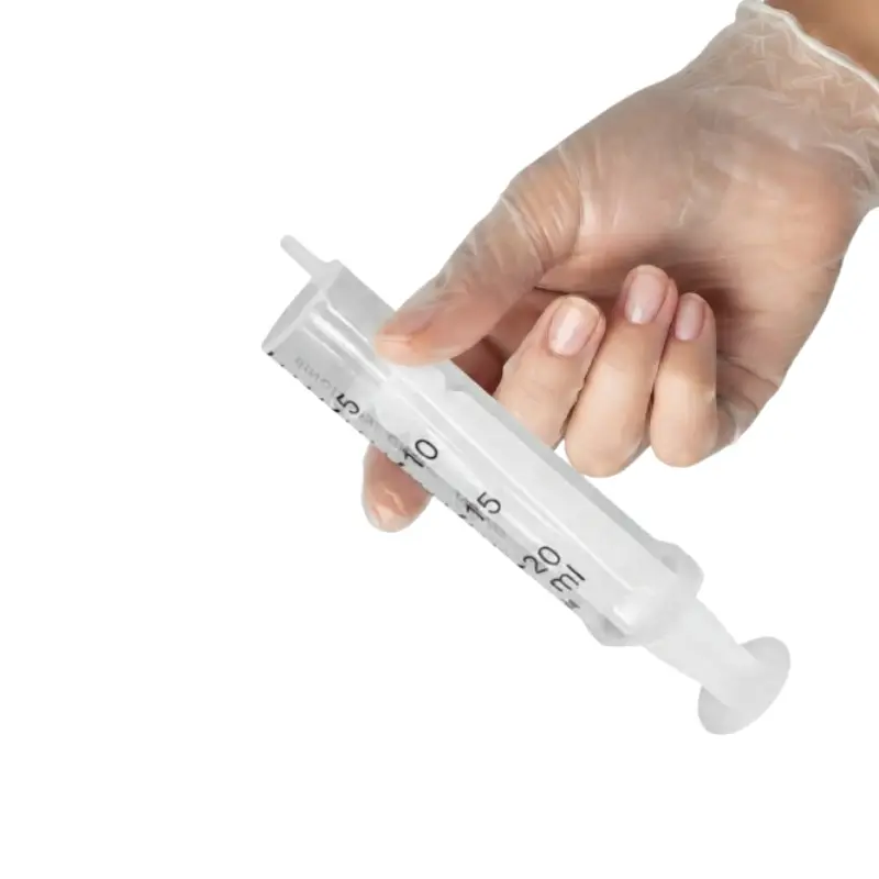 Mano con guante transparente sosteniendo una jeringa Nipro de 2 cuerpos y 20 ml para inspección clínica.