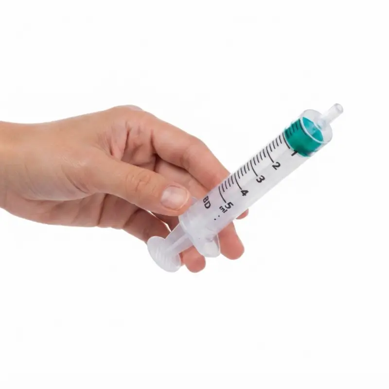 Mano sosteniendo una jeringa transparente de 3 cuerpos de 5 ml con émbolo verde sobre un fondo blanco aislado.