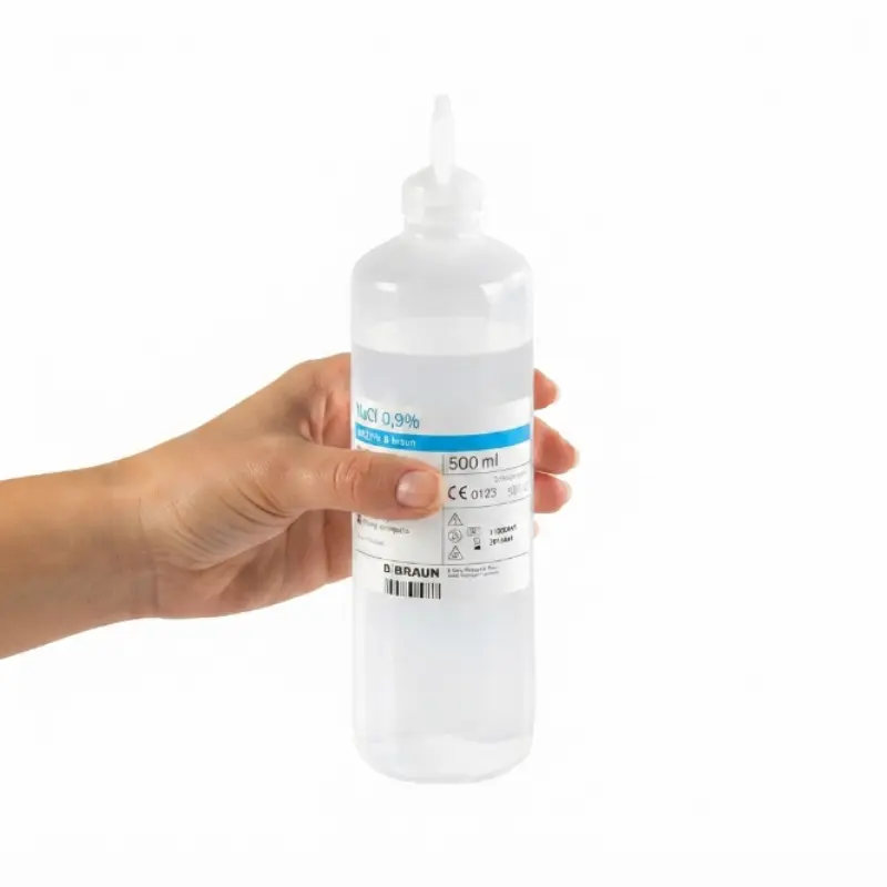 Mano de una persona sosteniendo un frasco de suero fisiológico estéril NaCl B. Braun de 500 ml sobre fondo blanco.