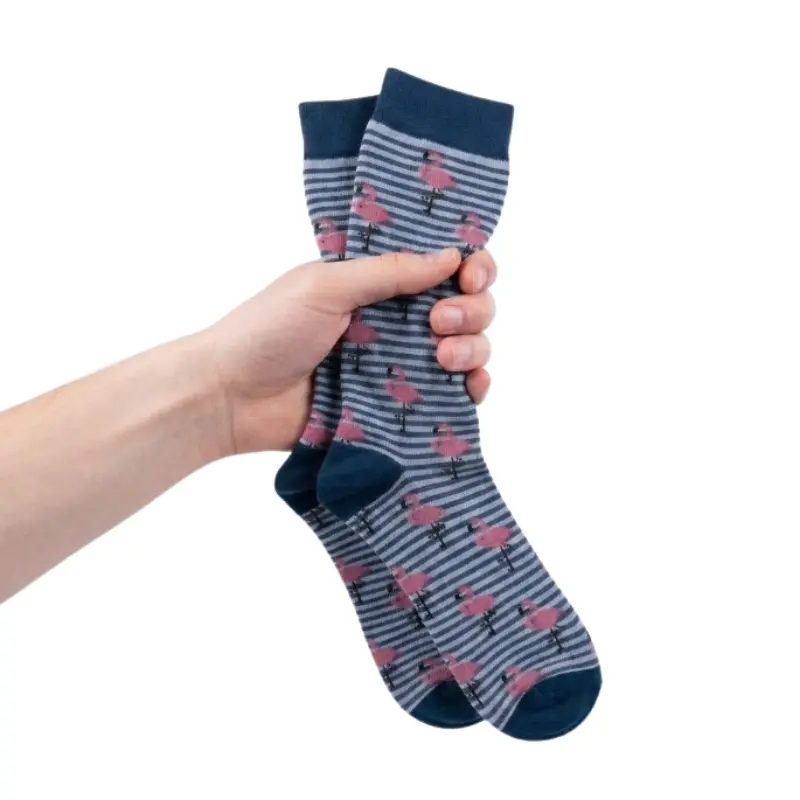 Mano humana sosteniendo un par de calcetines compresivos azul petróleo con estampado de flamencos rosas.