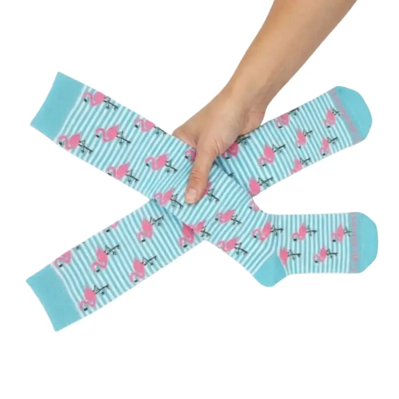 Mano humana sujetando dos calcetines compresivos turquesa cruzados con estampado de flamencos rosas.