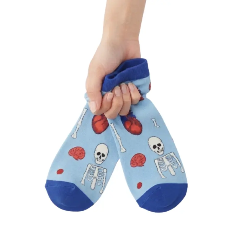 Mano sosteniendo un par de calcetines tobilleros celestes con estampado anatómico de esqueletos y corazones.
