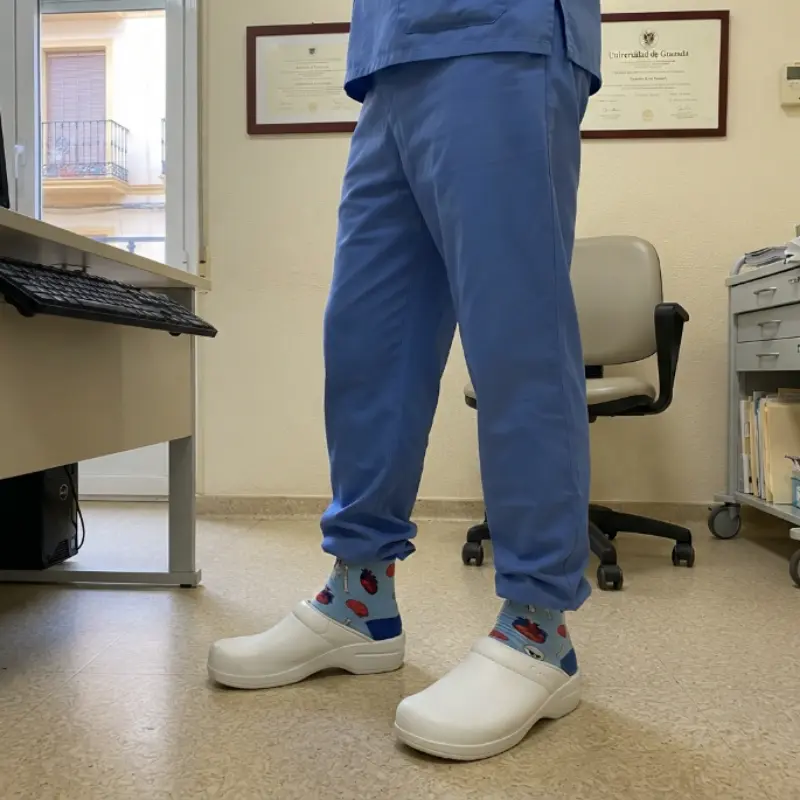 Profesional con pijama celeste y zuecos blancos luciendo los calcetines con estampado anatómico en la clínica.
