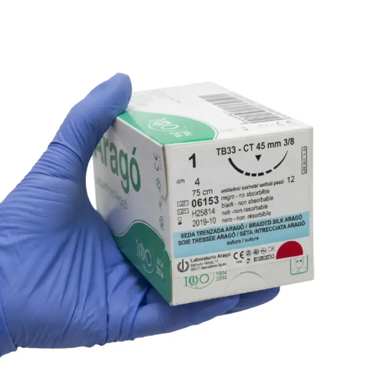 Mano con guante azul sosteniendo una caja de cartón de sutura no absorbible de seda Aragó.