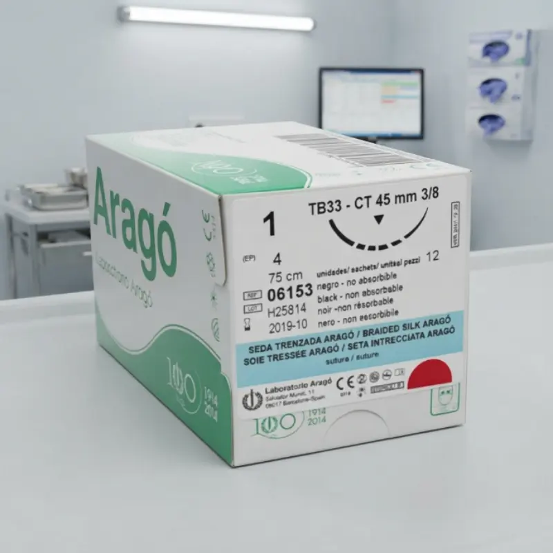 Caja de sutura no absorbible de seda Aragó apoyada sobre una superficie blanca frente a un monitor de ordenador en una clínica.
