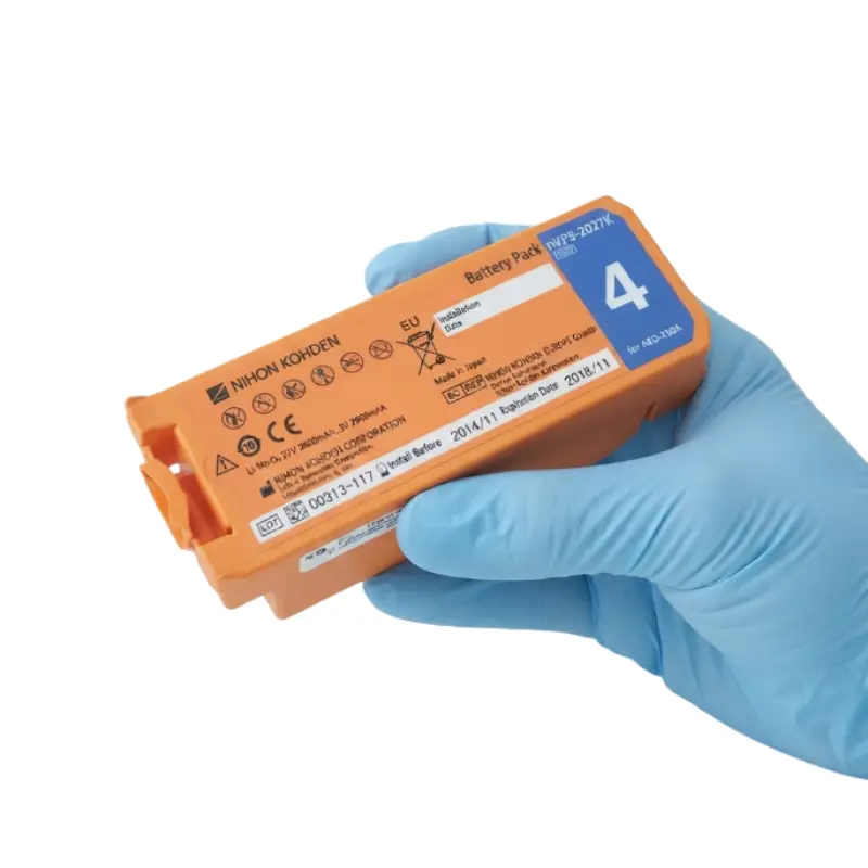 Mano con guante azul de nitrilo sosteniendo la batería naranja Nihon Kohden para desfibriladores AED-2100.
