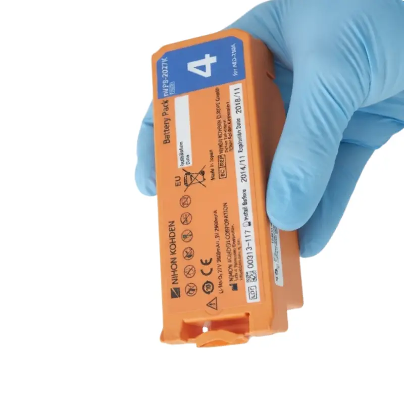 Mano con guante azul de nitrilo sosteniendo la batería naranja Nihon Kohden para desfibriladores AED-2100.