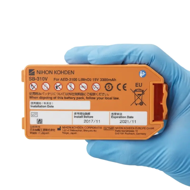 Mano con guante azul de nitrilo sosteniendo la batería naranja Nihon Kohden SB-310V para desfibrilador AED-3100.
