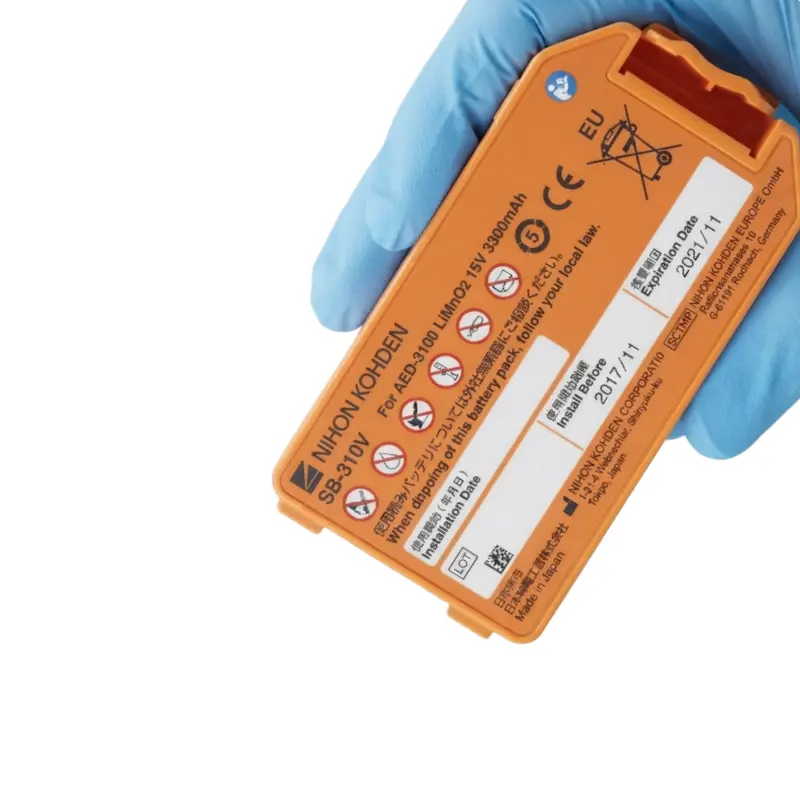 Mano con guante azul de nitrilo sosteniendo la batería naranja Nihon Kohden SB-310V para desfibrilador AED-3100.