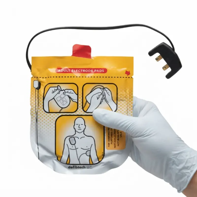 Mano con guante sanitario sujeta un envase de electrodos de adulto Defibtech Lifeline View con el conector superior visible.