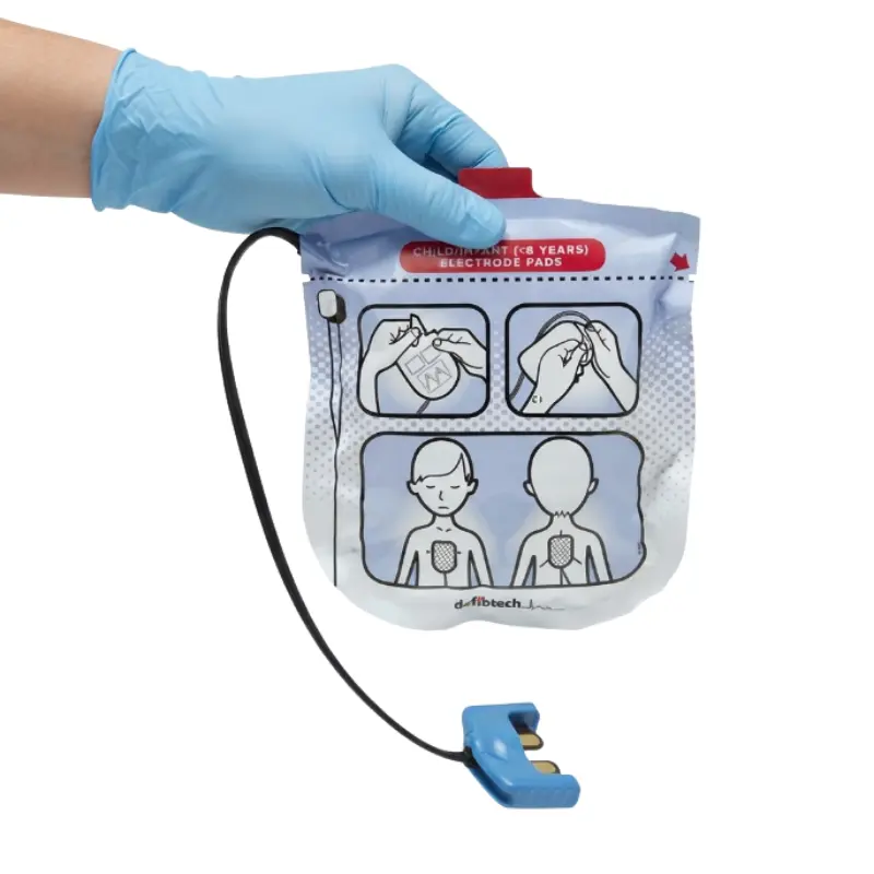Mano con guante azul sosteniendo el envase de los electrodos pediátricos Defibtech Lifeline View con el conector negro visible.