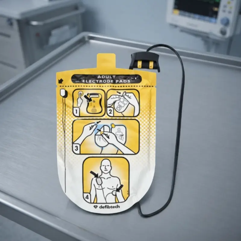 Envase de electrodos de adulto Defibtech Lifeline con cable y conector apoyado sobre una mesa clínica de acero inoxidable.