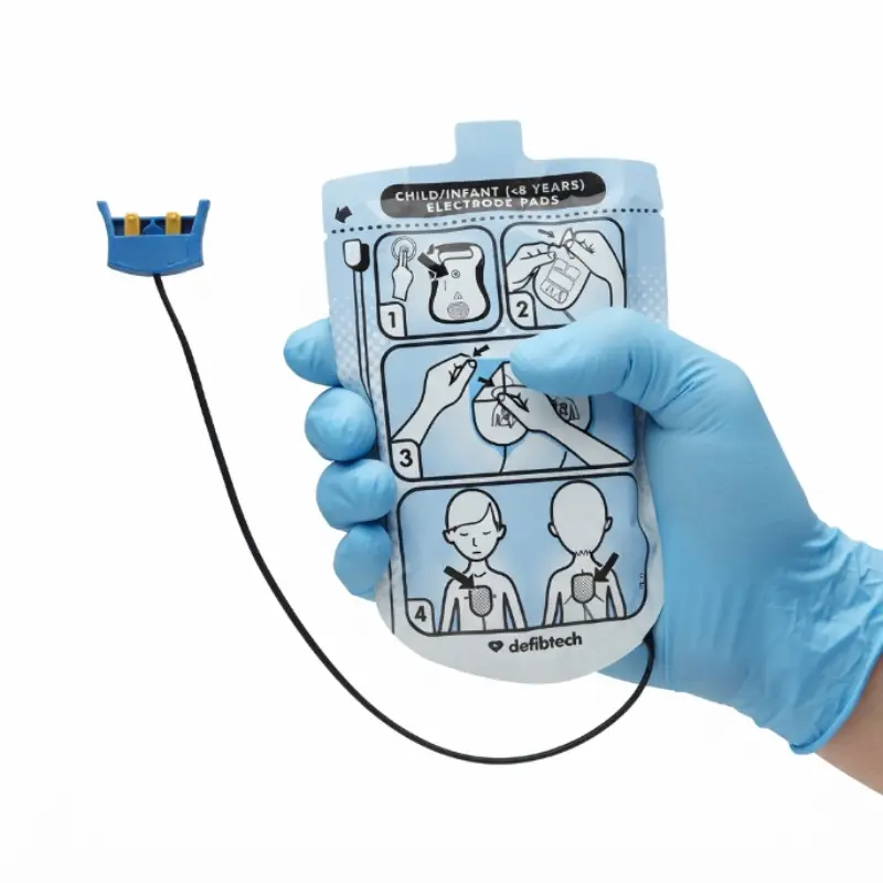 Mano con guante azul sujetando el sobre sellado de los electrodos pediátricos Defibtech Lifeline con conector azul.