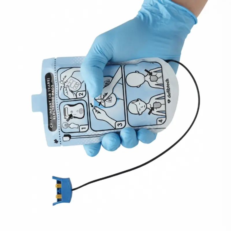 Mano con guante azul sujetando el sobre sellado de los electrodos pediátricos Defibtech Lifeline con conector azul.