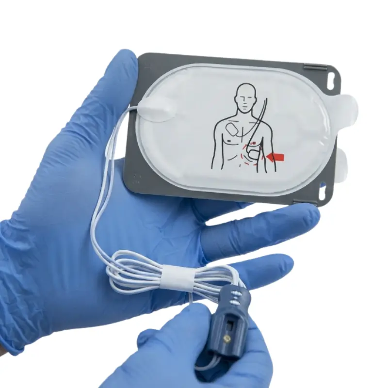 Manos con guantes azules sostienen los electrodos para adultos Philips Heartstart FR3 SMART III con cableado y conector.