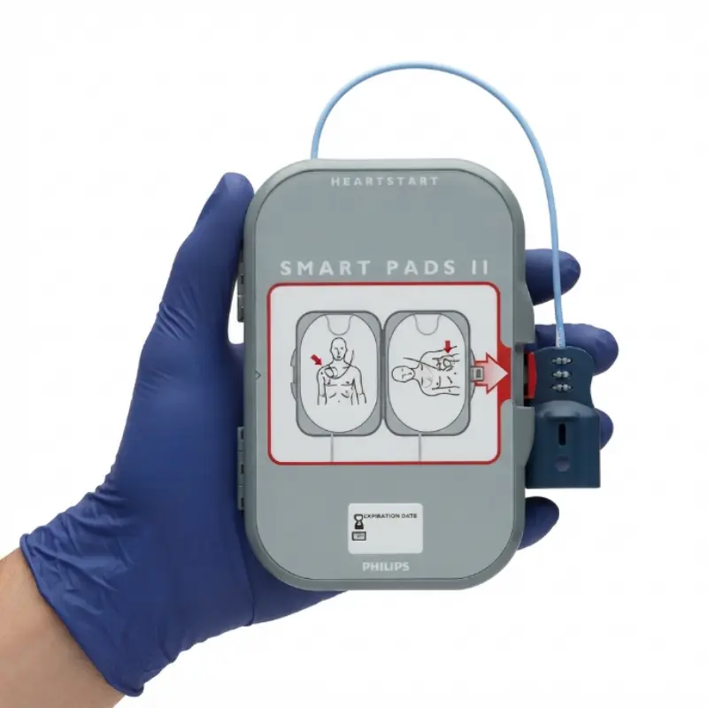 Mano con guante azul de nitrilo sosteniendo el cartucho gris de los electrodos Philips Heartstart FRx SMART II.