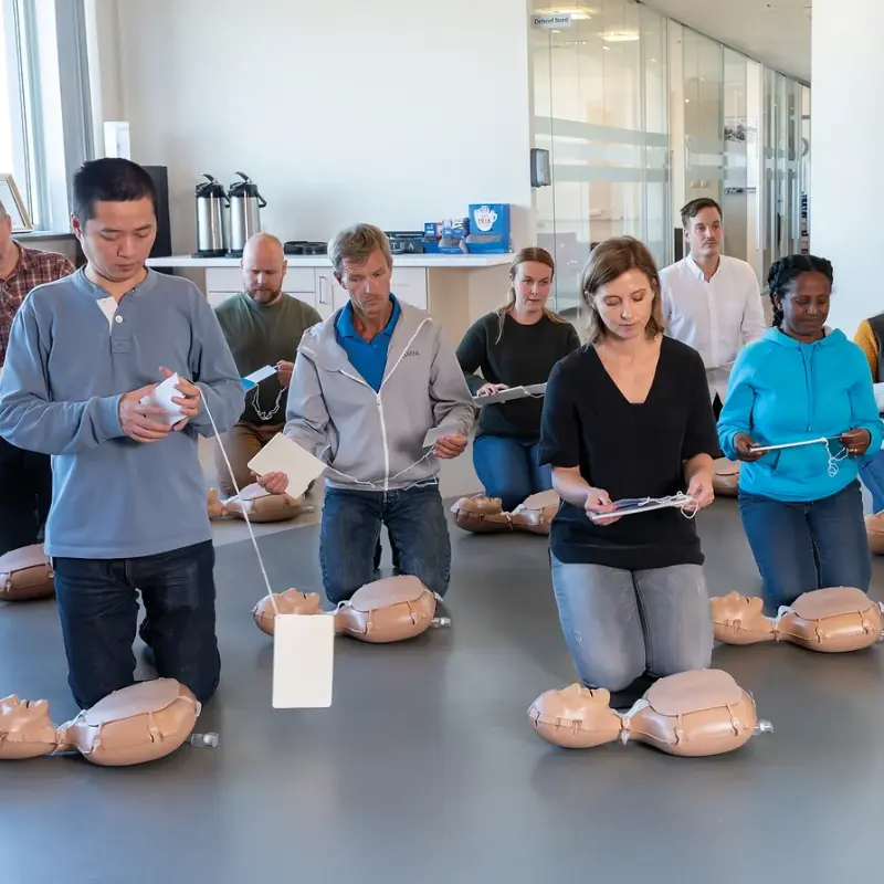 Grupo de profesionales sanitarios arrodillados sobre el suelo de una sala formativa practicando RCP con maniquíes de entrenamiento.