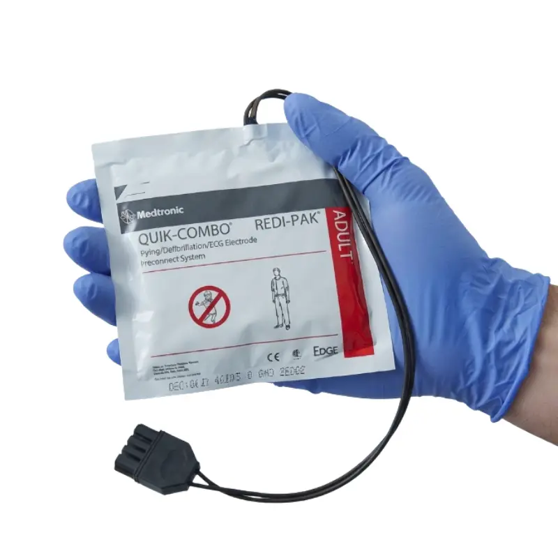 Mano con guante azul de nitrilo sosteniendo el sobre sellado de los Physio-Control Lifepak Quick-Combo electrodos adulto.